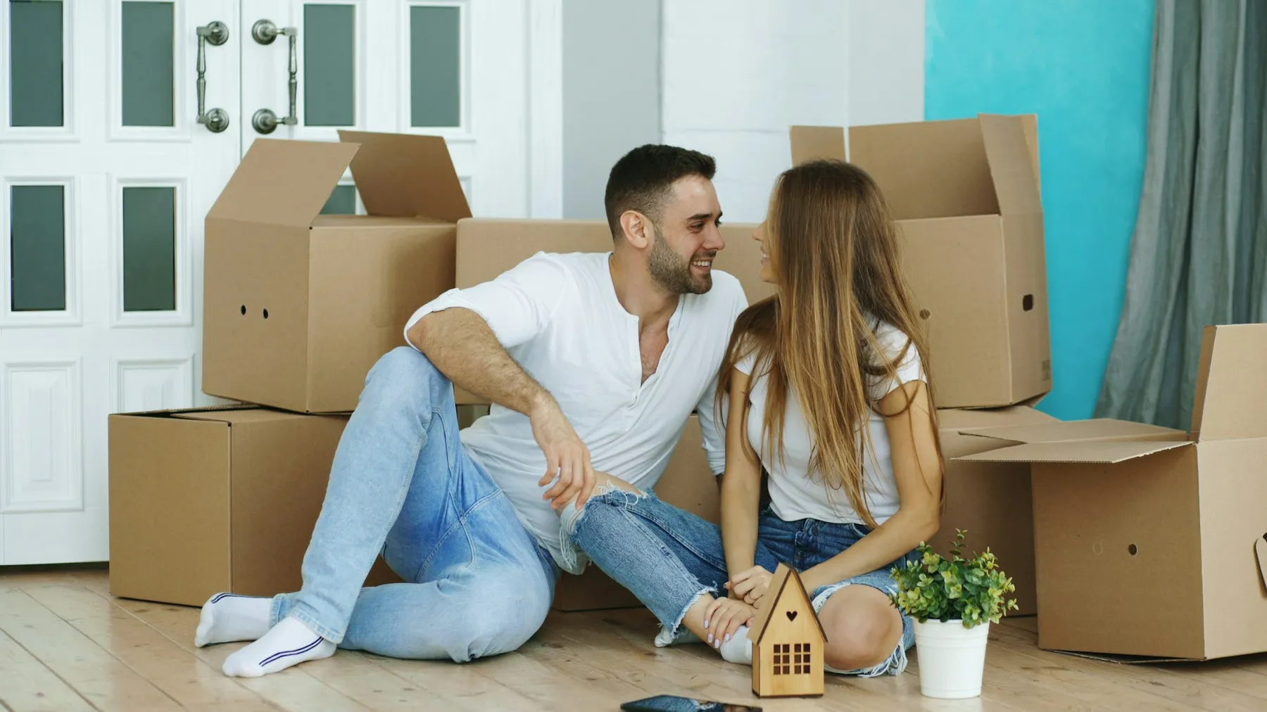 Couple laughing on the floor of their new home surrounded by moving boxes