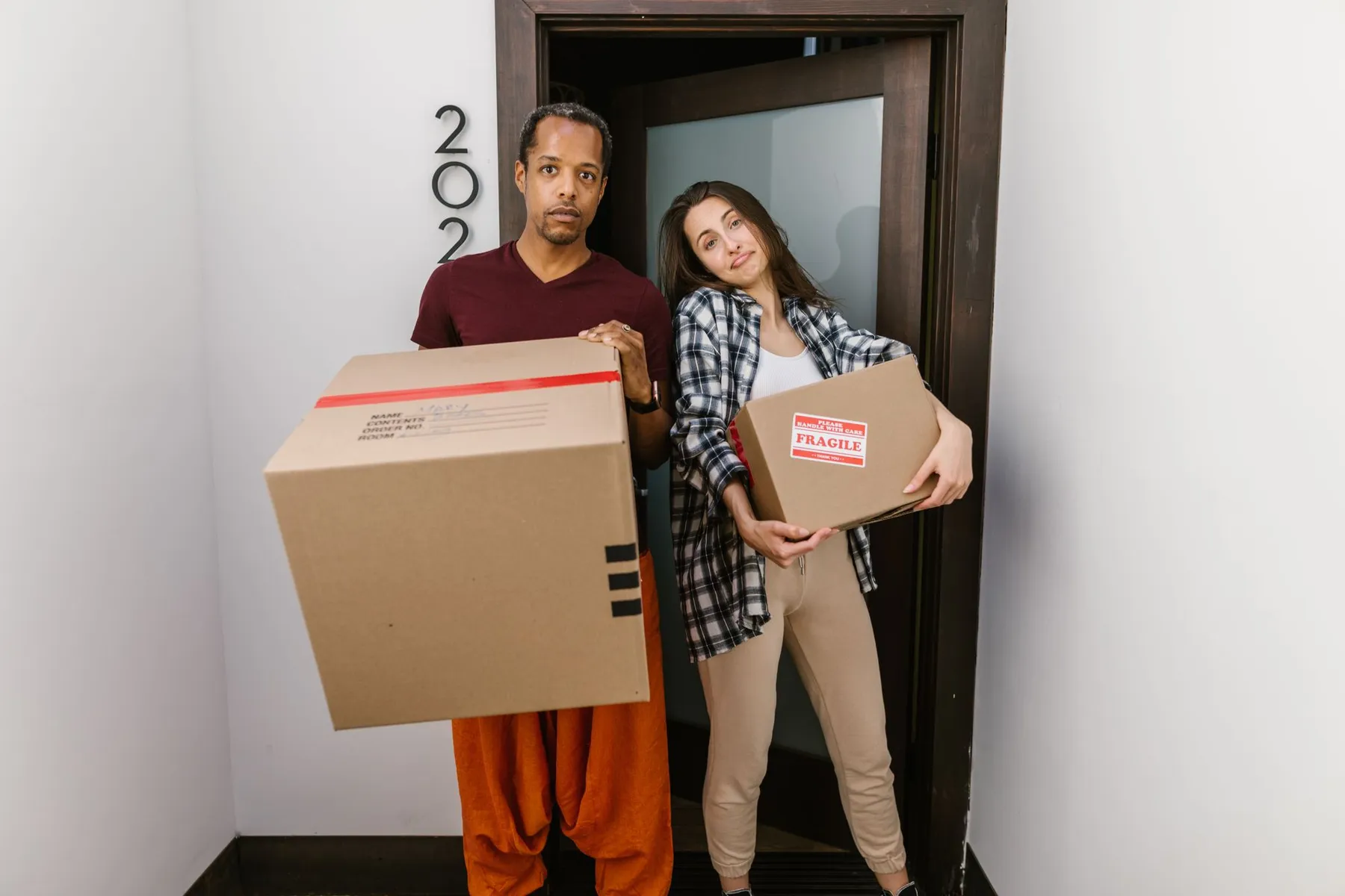 Couple standing in their new doorway carrying moving boxes