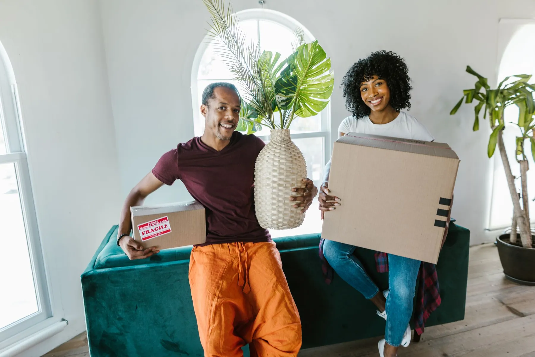 Smiling couple holding boxes and a plant in their new home